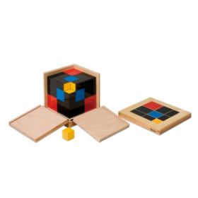 Συναρμολογημένος Τριωνυμικός Κύβος (Trinomial Cube) από πολύχρωμα ξύλινα κομμάτια (κόκκινο, κίτρινο, μπλε), τοποθετημένος μέσα σε ανοιχτό ξύλινο κουτί με δύο πλαϊνά κατεβασμένα. Στα δεξιά βρίσκεται το ξεχωριστό ξύλινο καπάκι με printed έγχρωμο σχέδιο. Στα αριστερά υπάρχουν δύο μεμονωμένα χαλαρά ξύλινα κυβάκια (ένα κόκκινο, ένα φυσικού ξύλου). Λευκό φόντο.