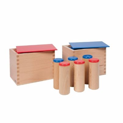Δύο ξύλινα κουτιά Nienhuis Montessori με κόκκινο και μπλε καπάκι, που περιέχουν έξι ξύλινους κυλίνδρους το καθένα, για την άσκηση της ακουστικής διάκρισης και της αντιστοίχισης ήχων.