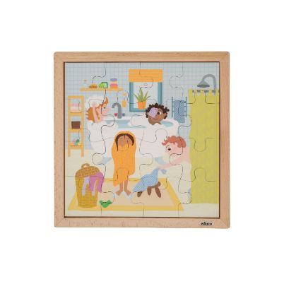 Μια λεπτομερής λήψη επίπεδης προβολής (flat lay) του πλήρως συναρμολογημένου ξύλινου παζλ Educo 90521 'Daily Routine - Bath Time'. Η εικονογράφηση δείχνει ένα πολυσύχναστο μπάνιο με τέσσερα διαφορετικά παιδιά που συμμετέχουν σε δραστηριότητες υγιεινής, όπως μπάνιο, στέγνωμα και αλλαγή ρούχων. Οι άκρες των 16 ξύλινων κομματιών είναι ορατές μέσα στο πλαίσιο. Το φόντο είναι απλό λευκό.